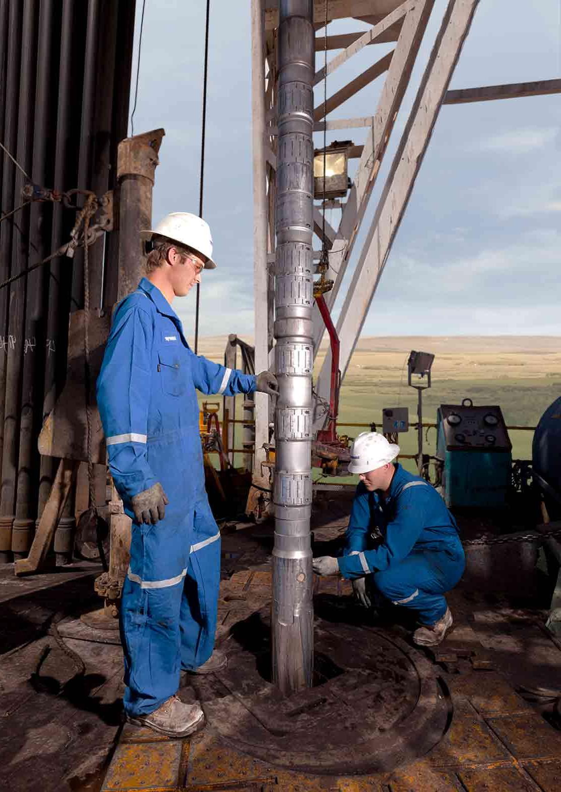 Two Schlumberger technicians adjust an LWD tool on a drilling rig floor